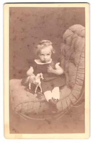 Fotografie Hermann Günter, Hannover, Marienstrasse 7, Kleinkind auf gepolstertem Stuhl mit Spielzeugpferd