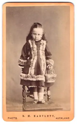 Fotografie R. H. Bartlett, Auckland, Kleines Mädchen im Mantel mit Korb