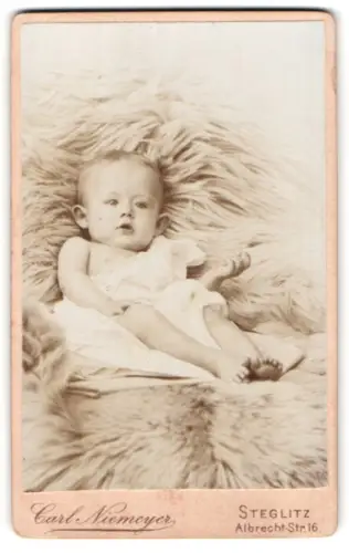 Fotografie Carl Niemeyer, Steglitz, Albrecht-Str. 16, Süsses Kleinkind im Hemd liegt auf Fell