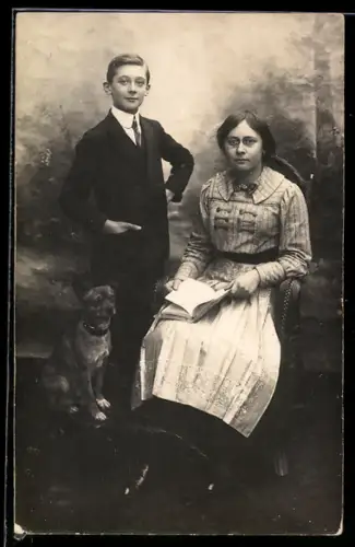 Foto-AK Hund, Knabe und Dame mit Buch vor Fotokulisse