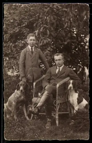 Foto-AK Knabe, zwei Jagdhunde und Herr in Reitstiefeln mit Gerte in einem Garten