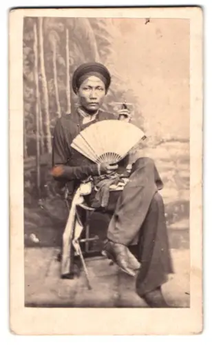 Fotografie unbekannter Fotograf und Ort, Porträt Vietnames /Annam mit Fächer vor Studiokulisse