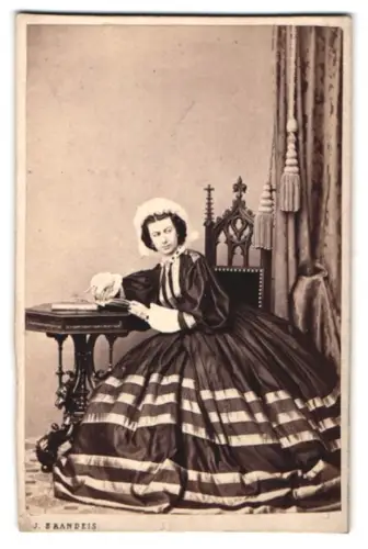 Fotografie J. Brandeis, Prag, Dame in elegantem Kleid an einem Tisch sitzend