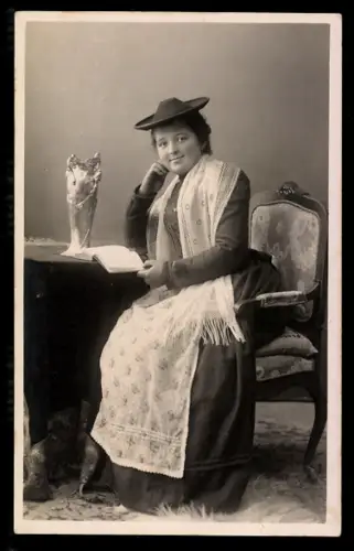 AK Frau in Tracht mit Hut an einem Tisch sitzend