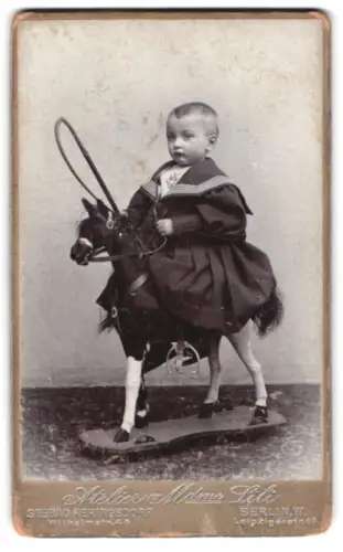 Fotografie Atelier Mdme Lili, Heringsdorf, Wilhelmstrasse 44, Kind in Matrosenkleid auf Spielzeugpferd