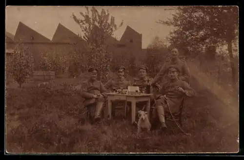 Foto-AK Soldatengruppe mit Diensthund an einem Tisch im Freien, Gebäude