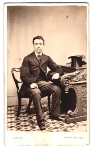 Fotografie M. Felton Cooper, London, Vornehm gekleideter Herr am Tisch