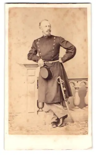 Fotografie unbekannter Fotograf und Ort, k.u.k. Offizier im Überrock mit Dienstmütze und Säbel