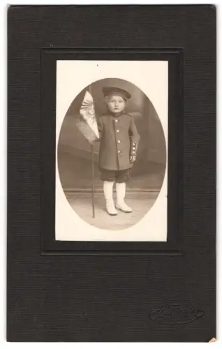 Fotografie A. Försters, Zwiesel, Kind im Waffenrock mit Krätzchen und Fahne
