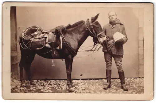 Fotografie unbekannter Fotograf und Ort, Bure mit Tropenhelm, Pistole am Halfter und gesatteltem Maultier, 1893