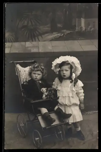 Foto-AK Kleines Mädchen mit kleinem Jungen im Kinderwagen vor einer Mauer