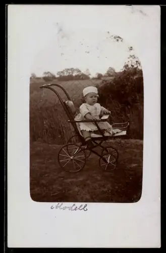 Foto-AK Kleinkind mit Kappe im Kinderwagen vor einem Maschendrahtzaun