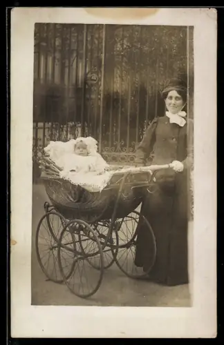 AK Dame mit Kleinkind im Kinderwagen vor einem eisernem Tor