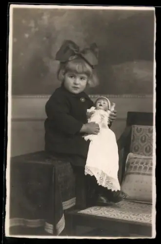 Foto-AK Kleines Mädchen mit Haarschleife hält Puppe im Arm