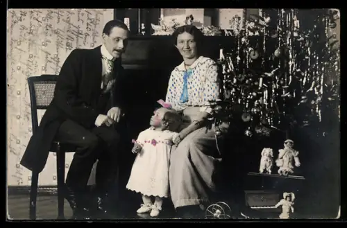 Foto-AK Familie sitzt am Weihnachtsbaum, Puppen als Geschenke unter dem Baum