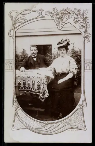 Foto-AK Paar an einem Tisch sitzend im Passepartout mit Stechpalme