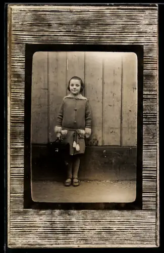 Foto-AK Mädchen im Mantel vor einer Wand stehend, Passepartout in Holzoptik