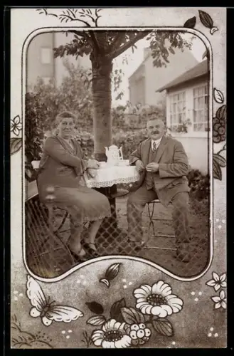 Foto-AK Paar an einem Tisch im Garten, Passepartout mit Blumen