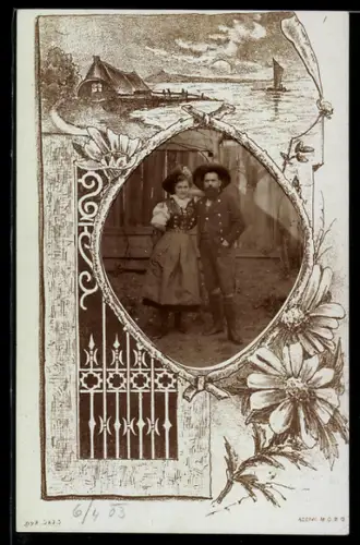 Foto-AK Trachtenpaar vor einer Bretterwand, Ast-Passepartout, Haus am Wasser, Gusseisenzaun, Blume