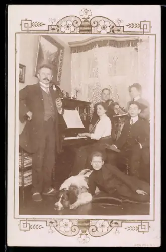 Foto-AK Gruppe mit Pianistin u. Berhardiner in einer Stube, Ornament-Passepartout
