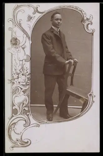 Foto-AK Junger Herr mit Stuhl, Ornament-Passepartout mit Engel
