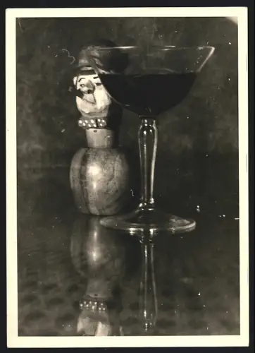 Fotografie Holzfigur mit Manneskopf neben einem Glas auf einem Tisch