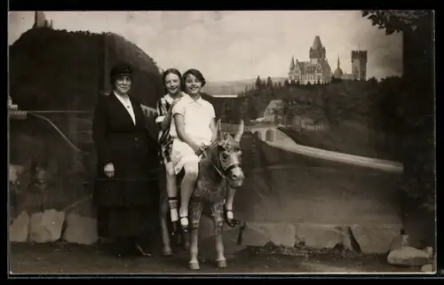 Foto-AK Dame mit zwei Mädchen auf einer Eselfigur vor idyllischer Studiokulisse