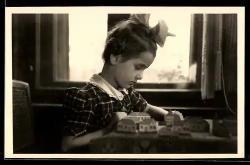 Foto-AK Kind mit Schleife im Haar vor einer Spielzeugstadt
