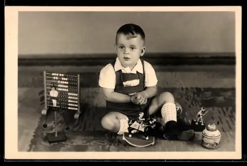 Foto-AK Kind mit diversen Spielzeugen auf dem Boden, darunter Reiter