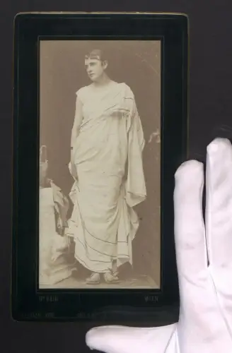 Fotografie Dr. Heid, Wien, Elegante Schauspielerin in antikem Kostüm neben einem Podest stehend