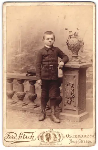 Fotografie Ferd. Nitsch, Osterode a. H., Neue-Strasse, Konrad Horman neben dekorativem Podest grüsst Tante Mathilde