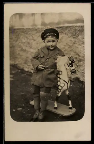 Foto-AK Junge im Mantel lehnt an einem Spielzeugpferd auf Rollen