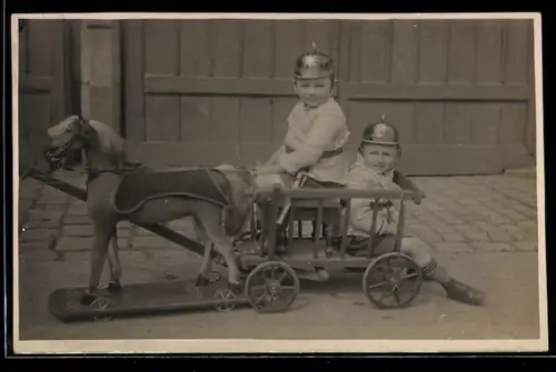 Foto-AK Zwei Jungen mit Feuerwehrghelmen in einer Kutsche mit Spielzeugpferd auf Rollen 1926