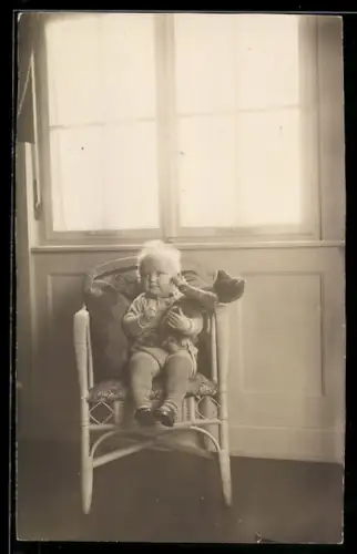 Foto-AK Kleinkind auf einem Stuhl hält einen Teddy im Arm