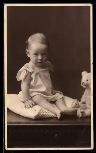 Foto-AK Kleinkind sitzt neben einem Teddy auf einem Kissen