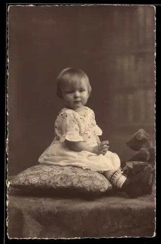 Foto-AK Kleinkind sitzt neben einem Teddy auf einem Kissen