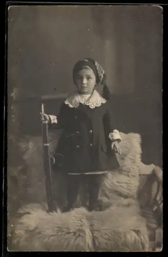 AK Kleinkind mit Spielzeuggewehr steht auf einem Stuhl mit Fell