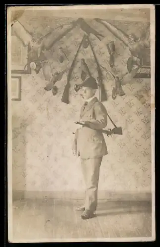 Foto-AK Jäger mit Gewehr vor Wand mit zahlreichen Jagdtrophäen, Jagd
