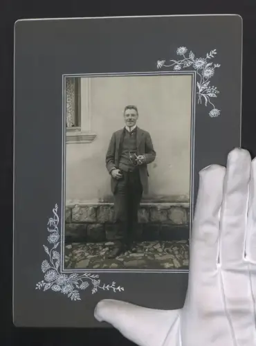 Fotografie unbekannter Fotograf und Ort, Portrait eines lächelnden Mannes mit Zigarette an einer Hauswand, 18 x 25cm