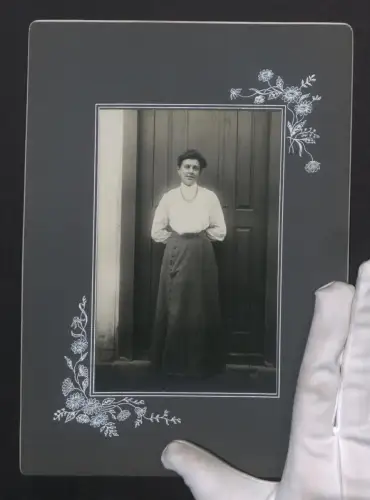 Fotografie unbekannter Fotograf und Ort, Portrait einer lächelnden Frau mit Kette vor einer Tür, Grossformat 18 x 25cm