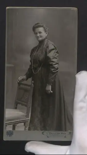 Fotografie L. Grillich, Wien, Wiedner Hauptstr. 12, Portrait einer Frau im eleganten Kleid mit Halskette an einem Stuhl