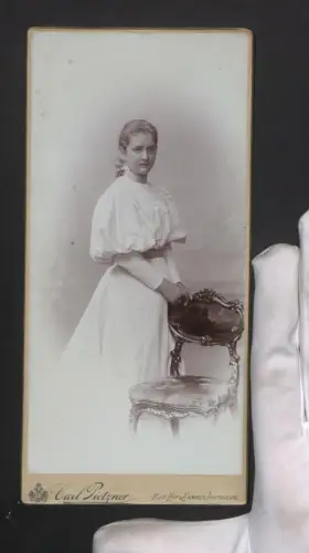 Fotografie Carl Pietzner, Wien, Mariahilferstrasse 3, Elegante Dame im weissen Kleid neben einem Stuhl im Portrait
