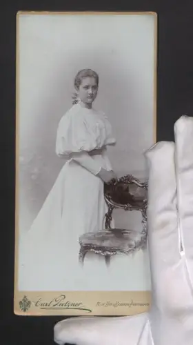 Fotografie Carl Pietzner, Wien, Mariahilferstrasse 3, Elegante Dame im weissen Kleid neben einem Stuhl im Portrait