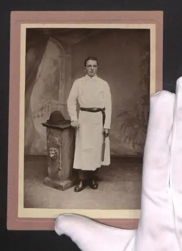 Fotografie Portrait eines jungen Mannes in Metzger-Arbeitskleidung neben einer Säule mit Hut