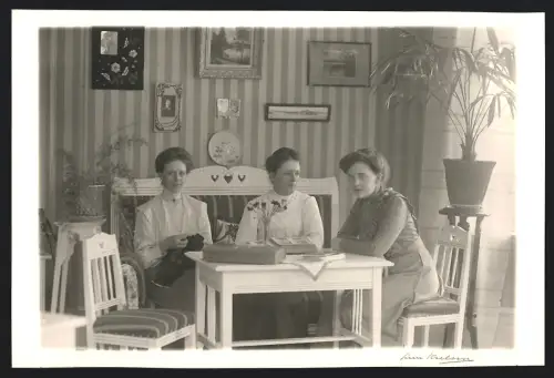 Fotografie unbekannter Fotograf und Ort, Drei Damen sitzen an einem Tisch mit Blumenvase und Bildern an der Wand