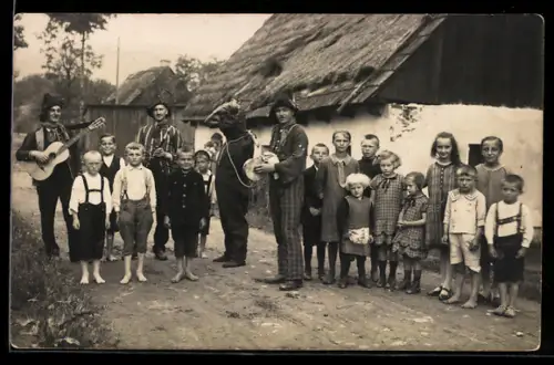 Foto-AK Artistengruppe mit als Bär Verkleidetem mit Kindergruppe auf einer Dorfstrasse, Gitarre, Klarinette