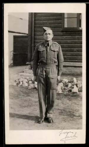 Foto-AK Britischer Soldat in Uniform mit Feldmütze vor einer Wohnbaracke