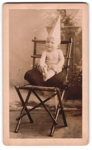Fotografie unbekannter Fotograf und Ort, Arnold Steiger als der kleine Lausbub, Kind mit spitzem Hut auf einem Stuhl