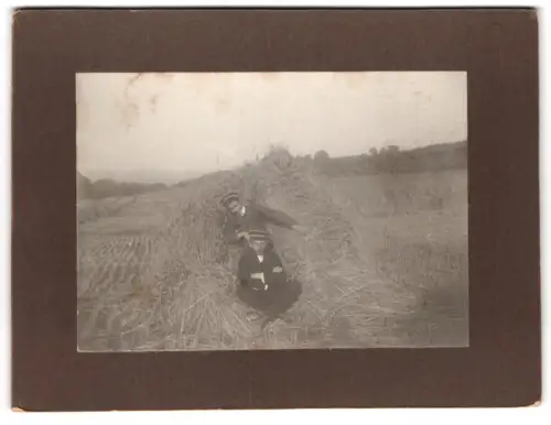 Fotografie unbekannter Fotograf und Ort, Zwei Studenten mit Tellermützen in einem Getreidehaufen