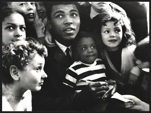 Fotografie Boxer Muhammad Ali mit einem Kleinkind auf dem Schoss und umgeben von anderen Kindern, Grossformat 25 x 19cm